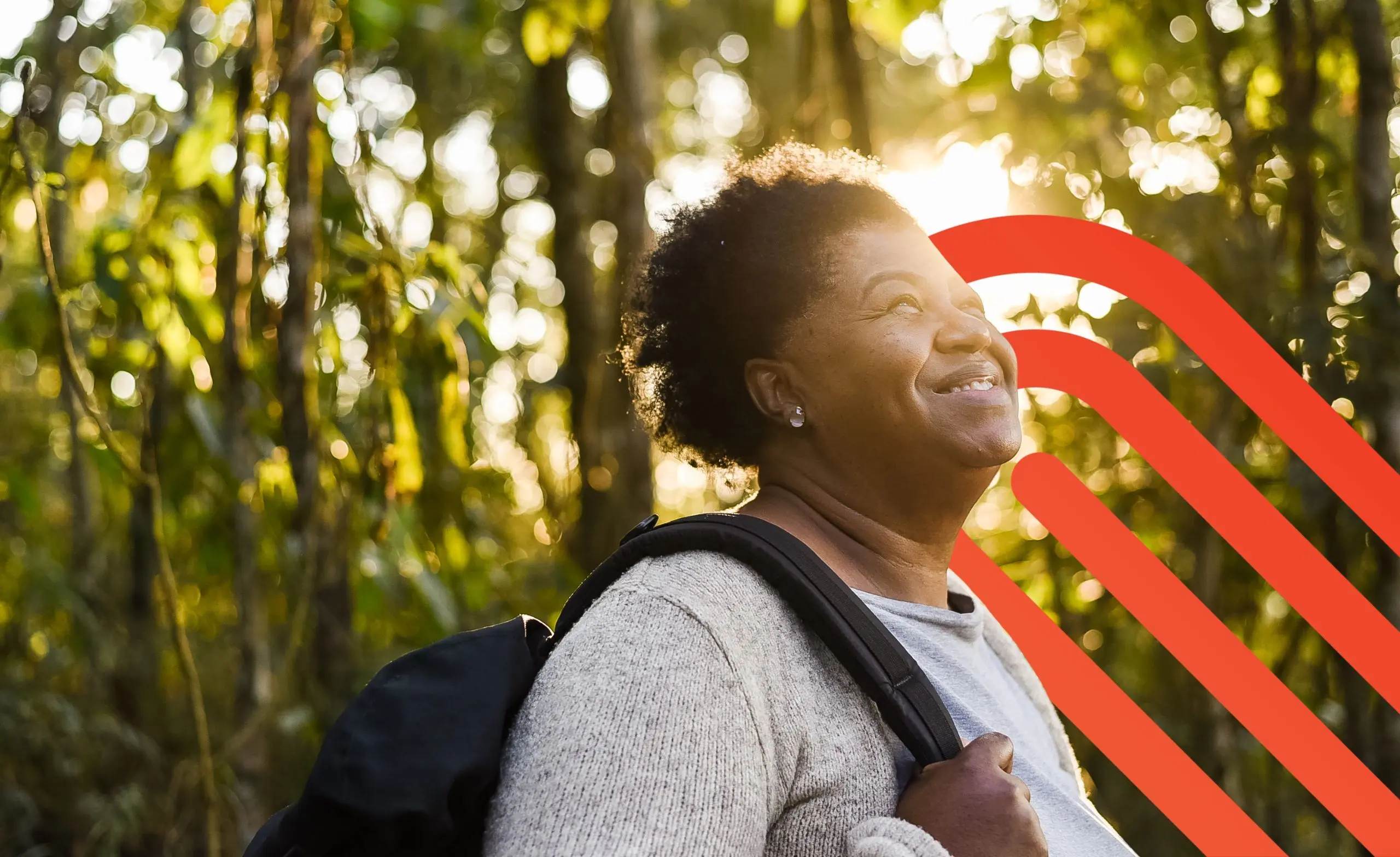 Woman with a backpack walking in the forest and smiling up at the sun